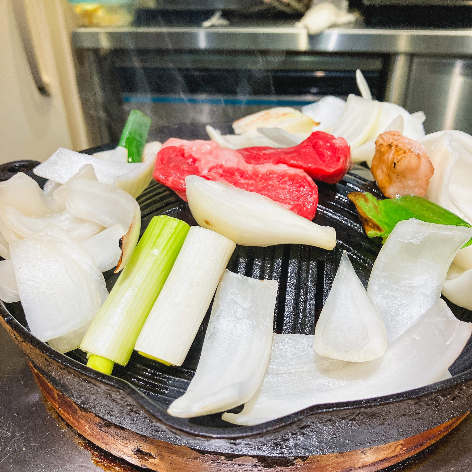 玉ねぎと長ねぎを載せたジンギスカン鍋で焼く羊肉
