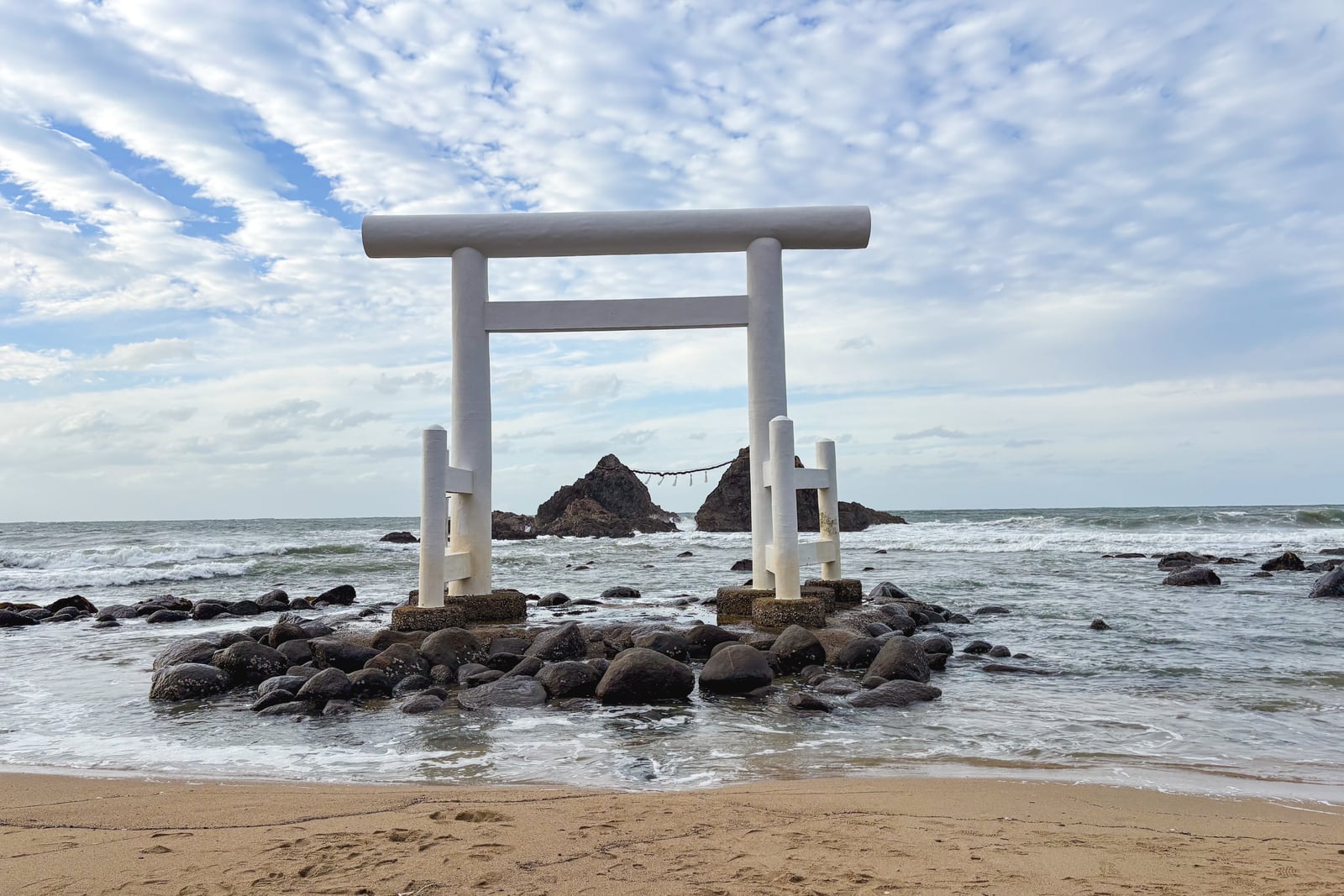 西の浦の海辺の岩場に立つ白い鳥居