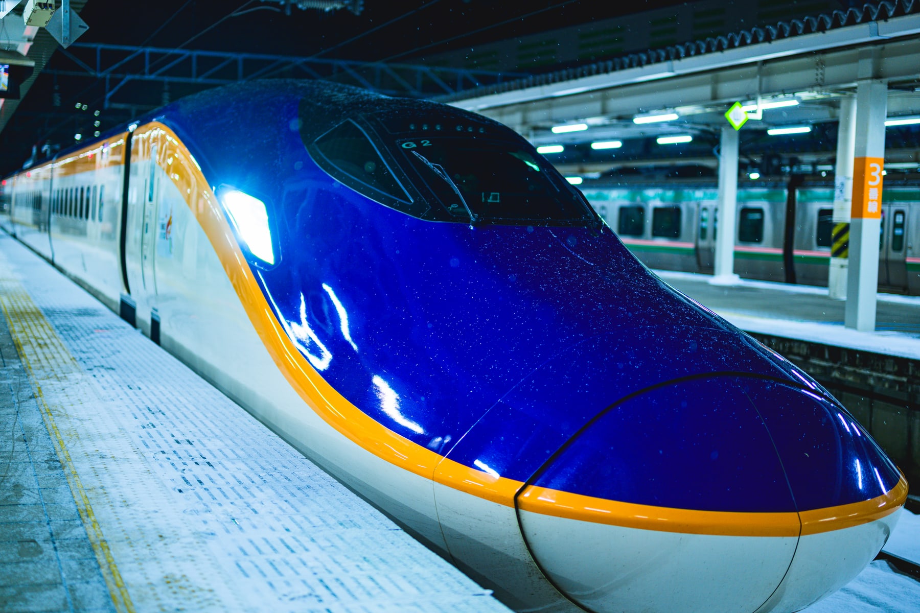 雪が降るホームに停車する青とオレンジ色の新幹線