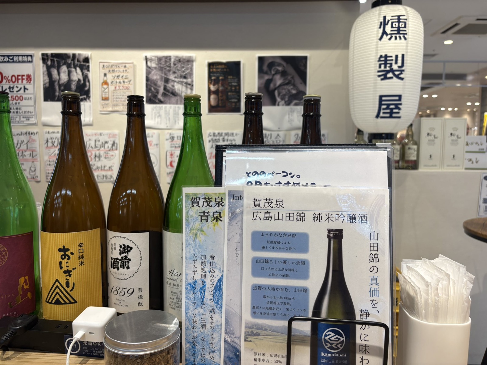 とののベーコン。広島 ekie 店に並ぶ日本酒の瓶と、燻製屋と書かれた提灯