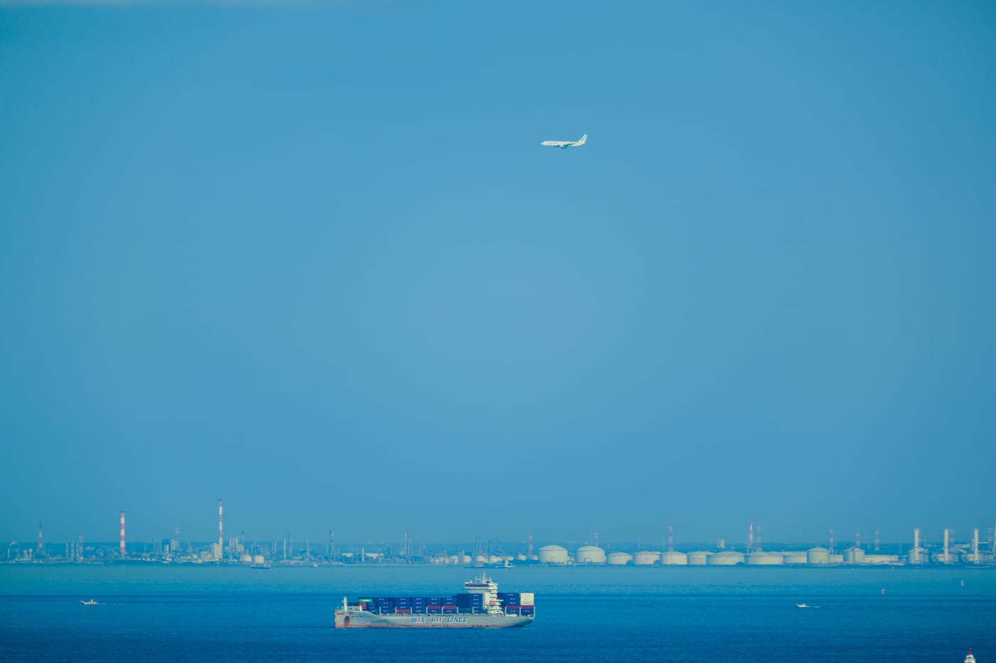 Ships crossing blue Tokyo Bay with an airplane in the distance