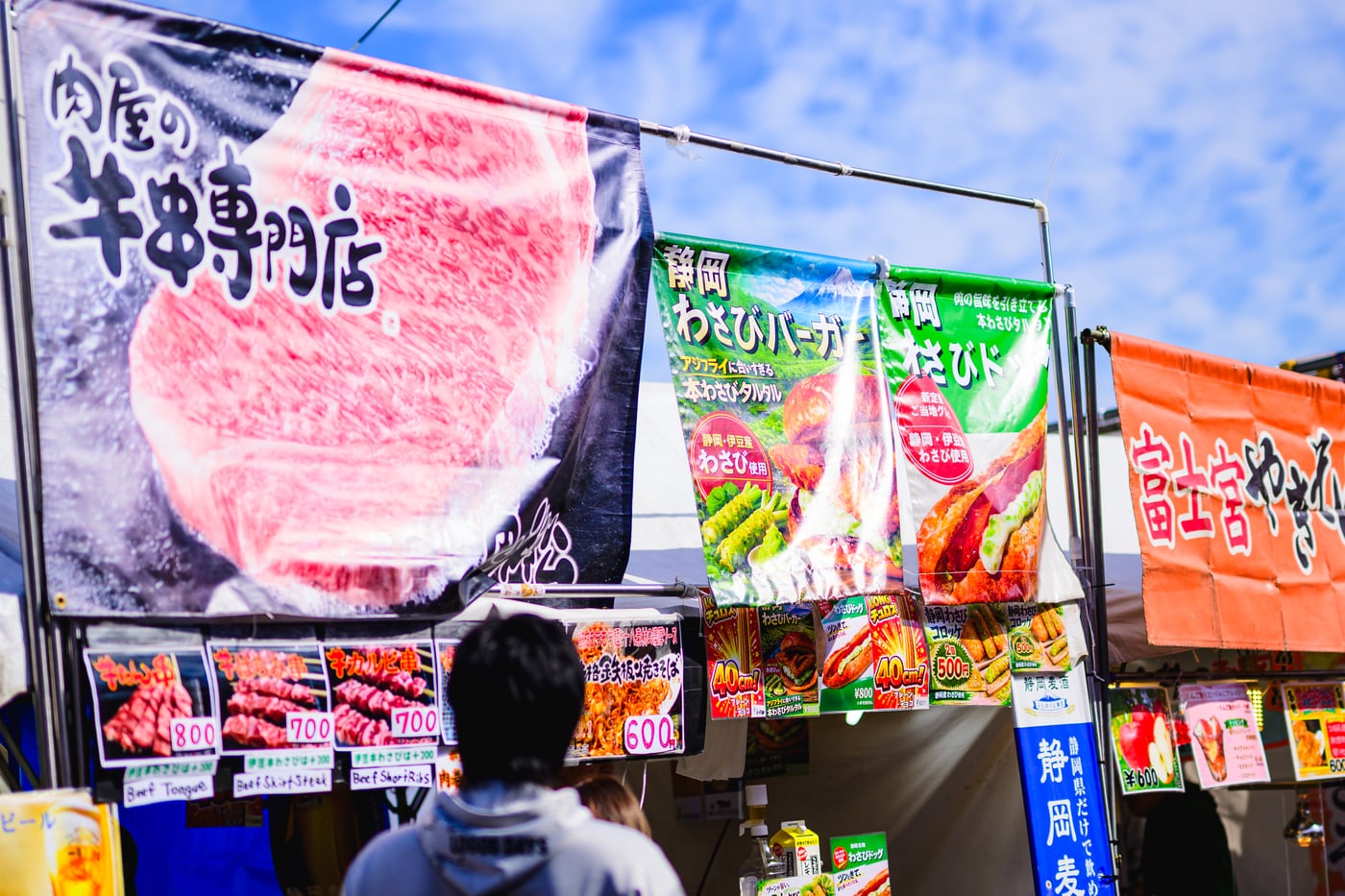 Festival food stalls with signs for beef skewers, wasabi burgers, and Fujinomiya yakisoba