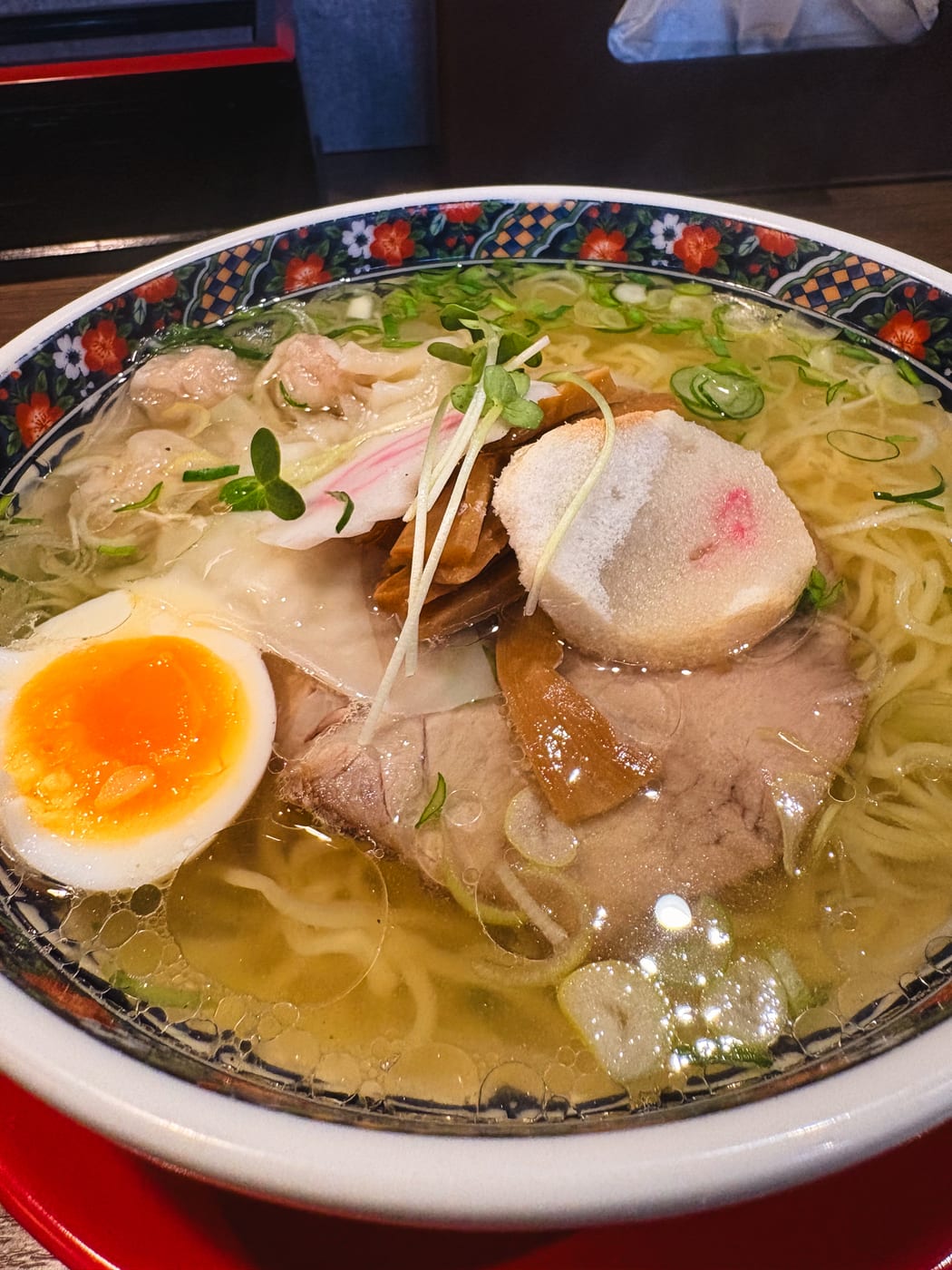 Ramen with wontons, chashu, and a seasoned egg in a clear salt-based broth