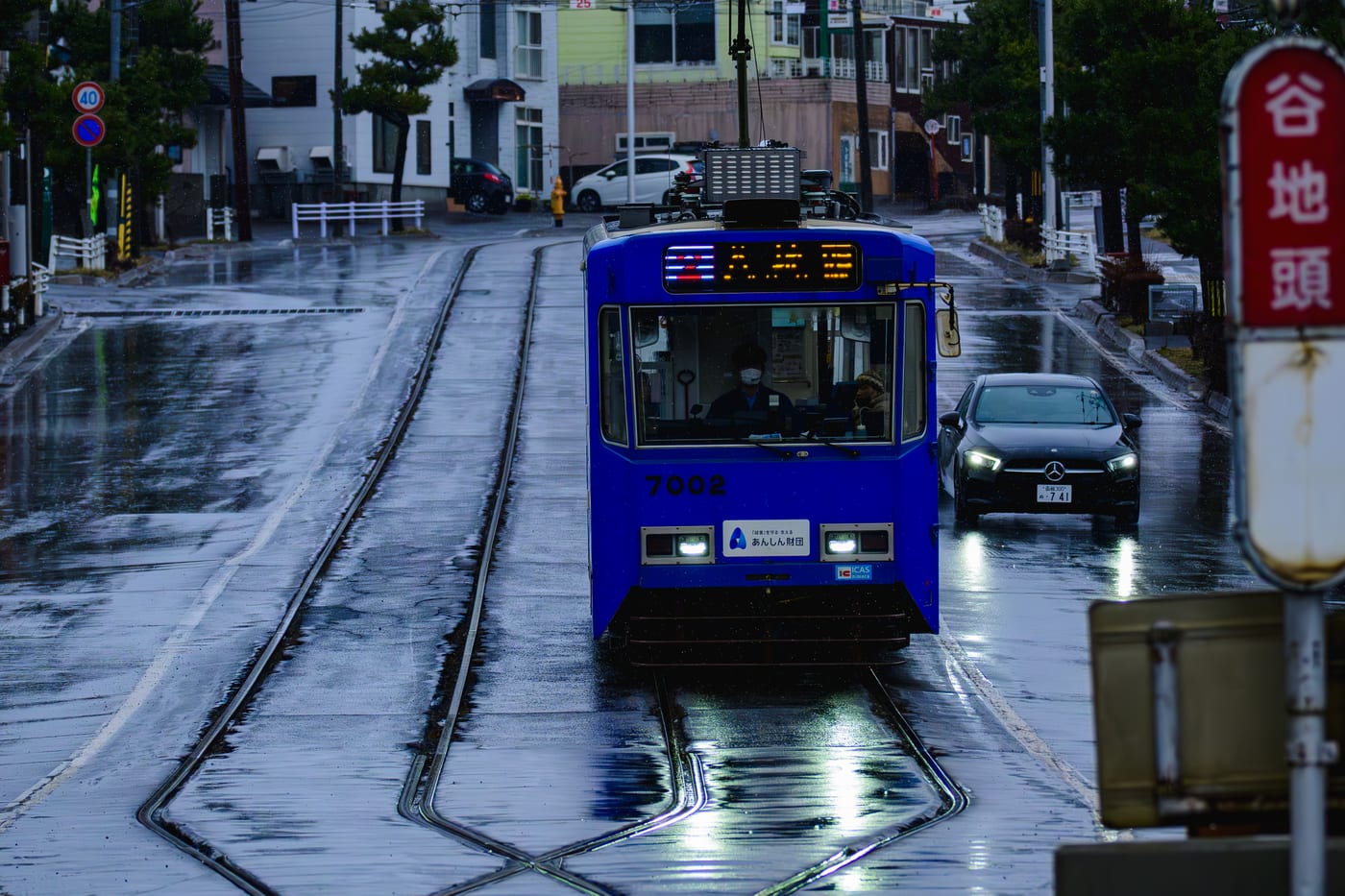 A blue Hakodate streetcar approaching head-on along rain-wet tracks