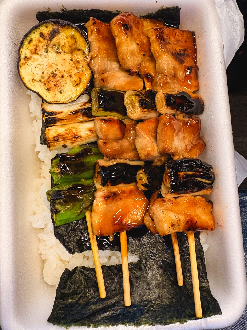 A Hasegawa Store yakitori bento with pork and vegetable skewers arranged over rice