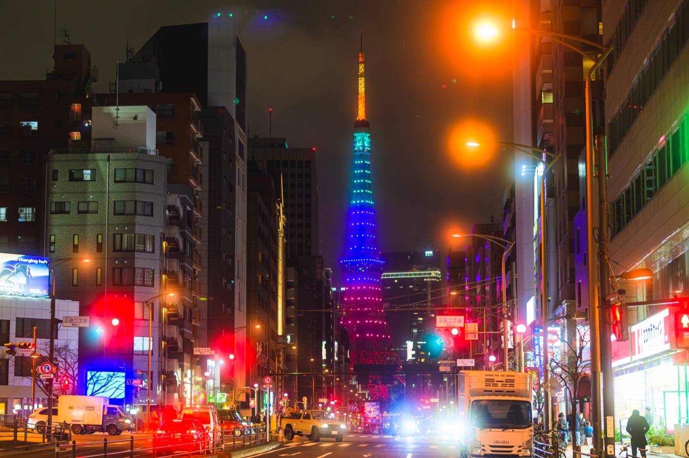 Tokyo Tower glowing in several colors beyond the nighttime city streets