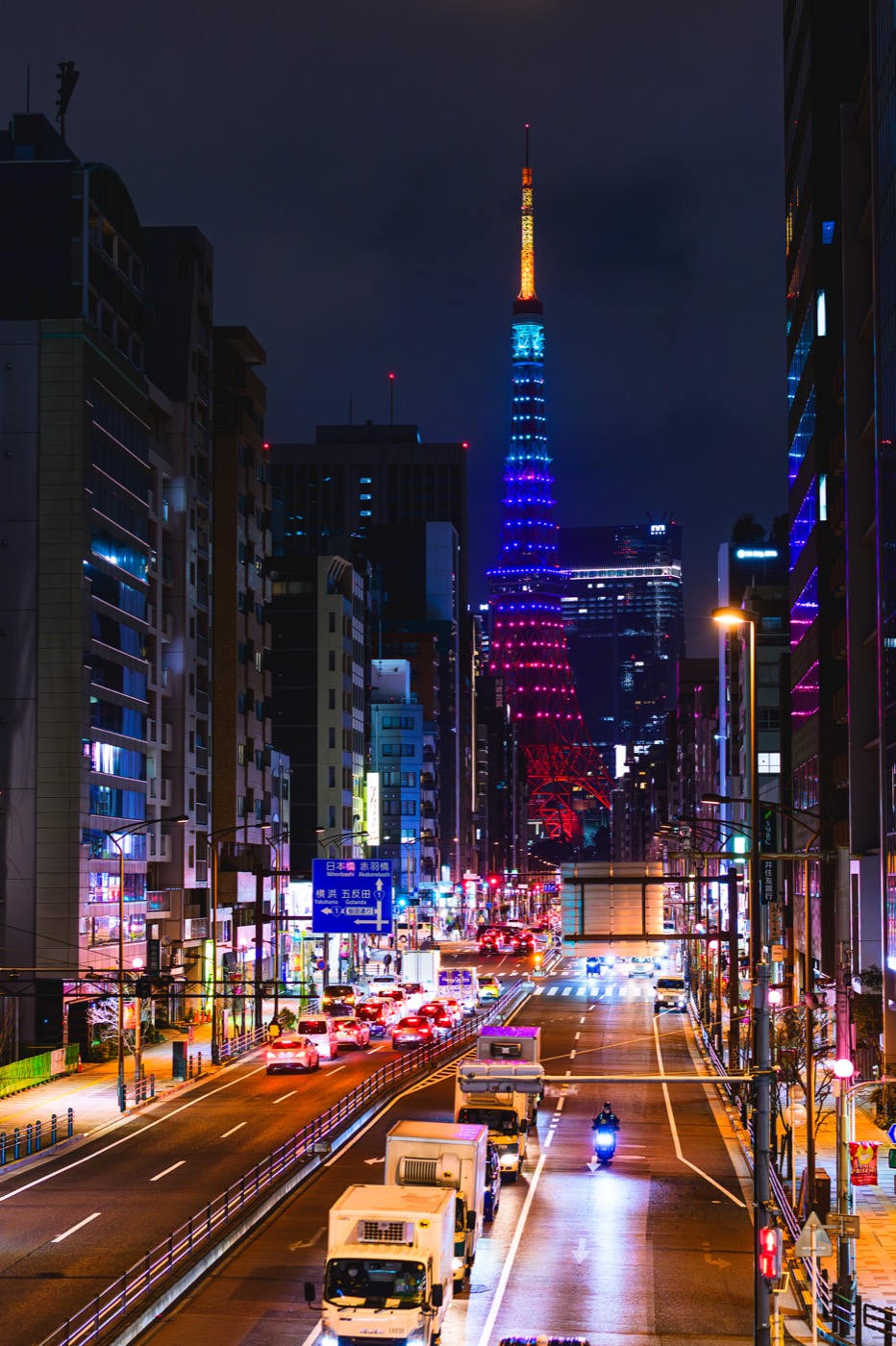 Tokyo Tower in MISAMO colors beyond nighttime traffic on a street in Mita