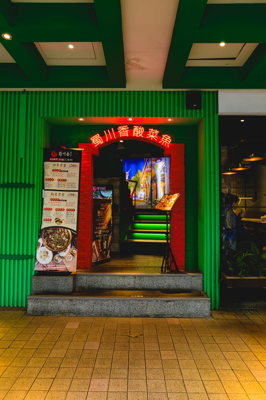 The entrance to Shuchuanxiang Suancai Fish, with a green exterior wall and red neon lights