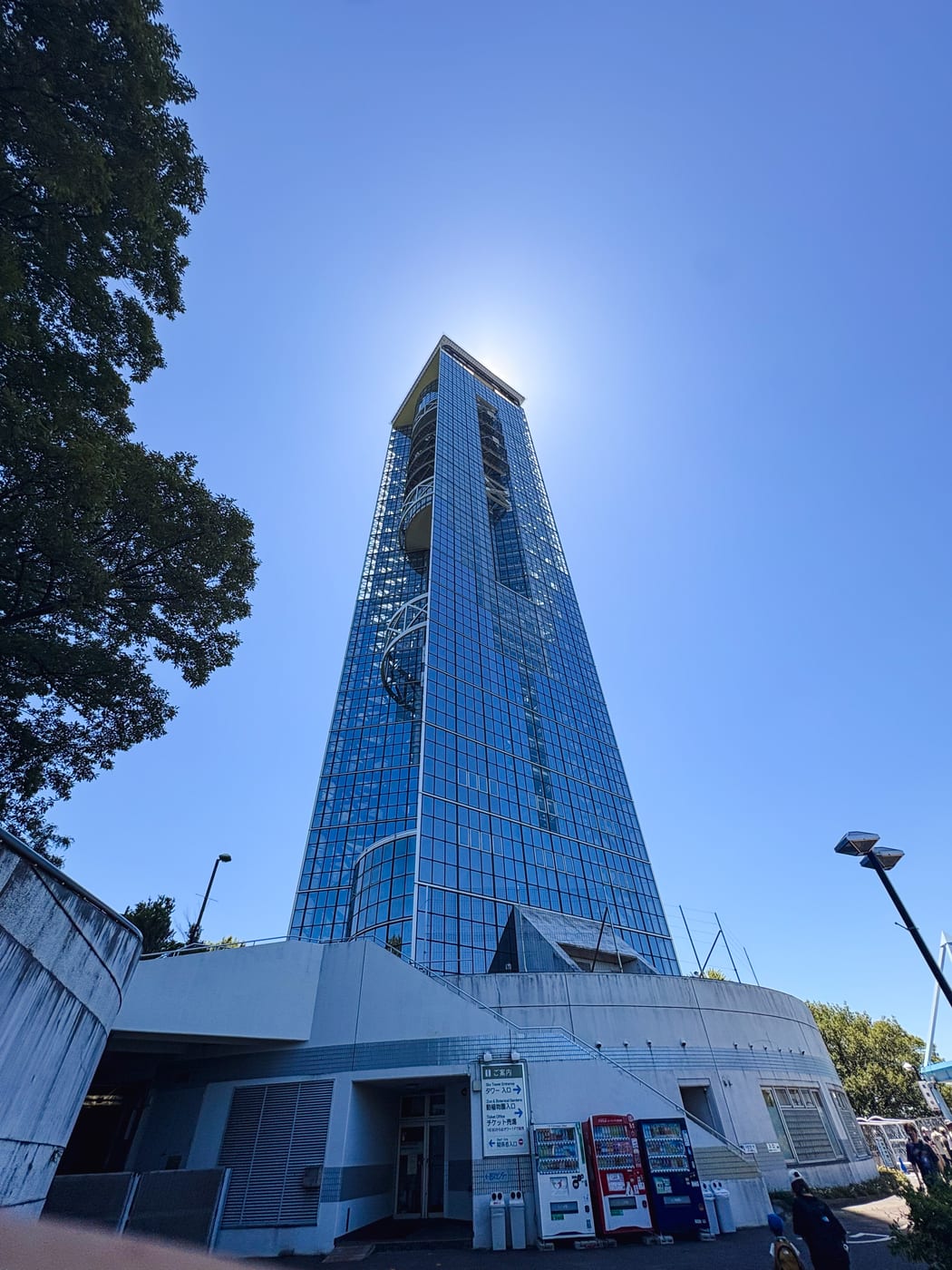 Higashiyama Sky Tower rising into a blue sky between trees