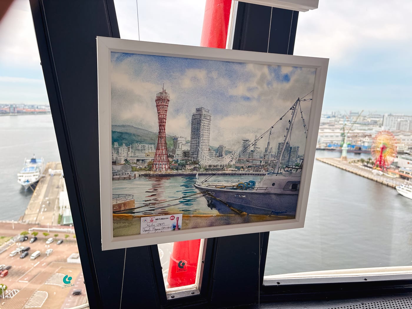 A painting of old Kobe Port and Port Tower displayed inside Kobe Port Tower, with the current harbor and red steel frame visible behind it