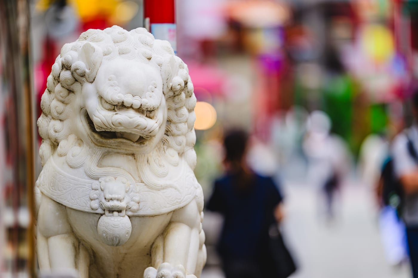 A white komainu statue with a Nankinmachi street in the background