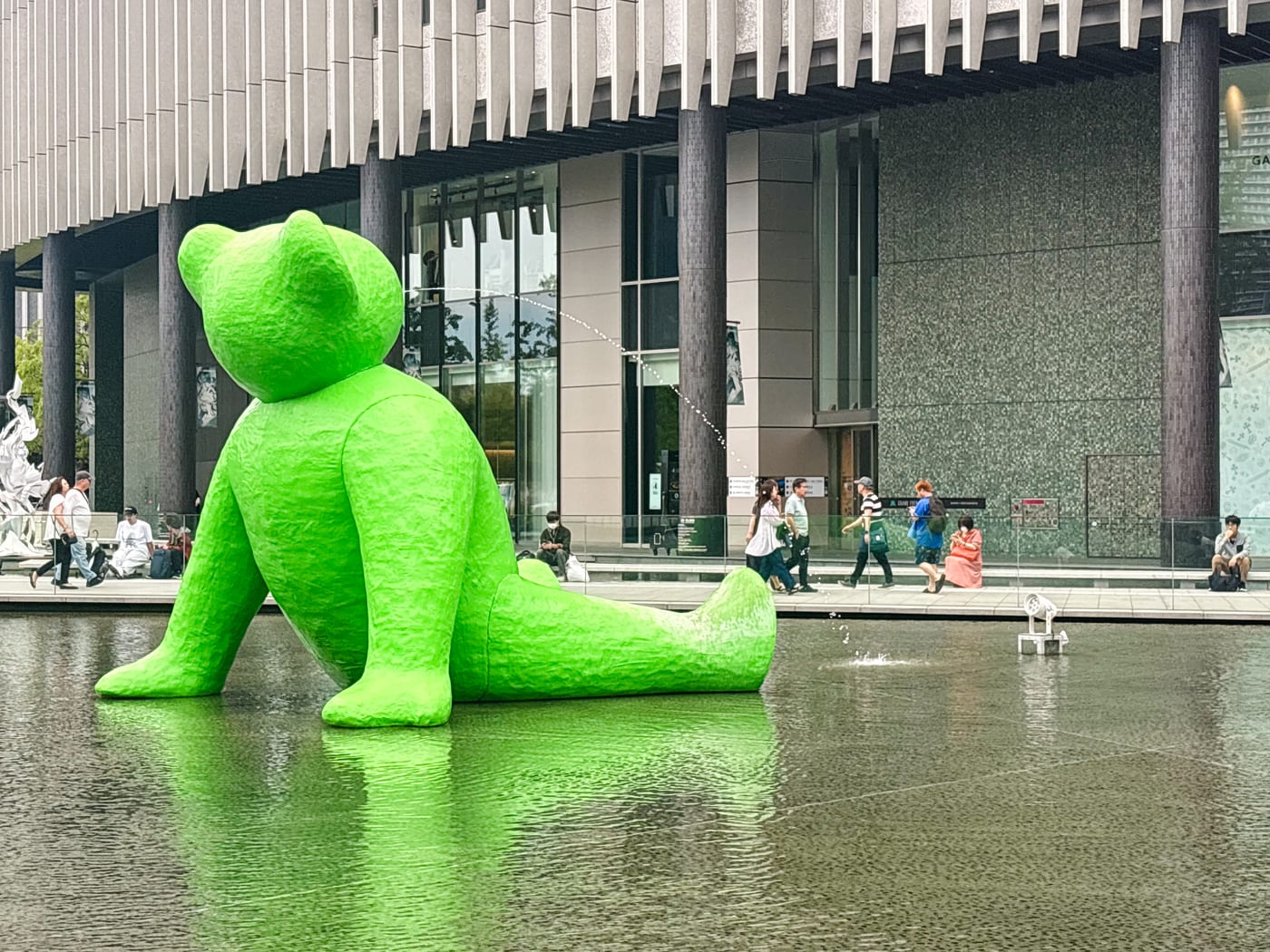A large green bear sculpture sitting beside water in front of Osaka Station