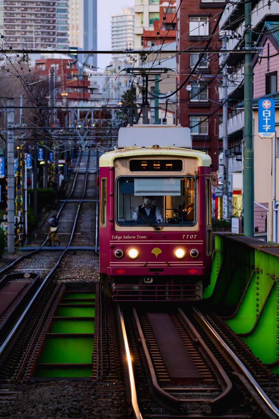 A burgundy tram crossing a green bridge and approaching head-on