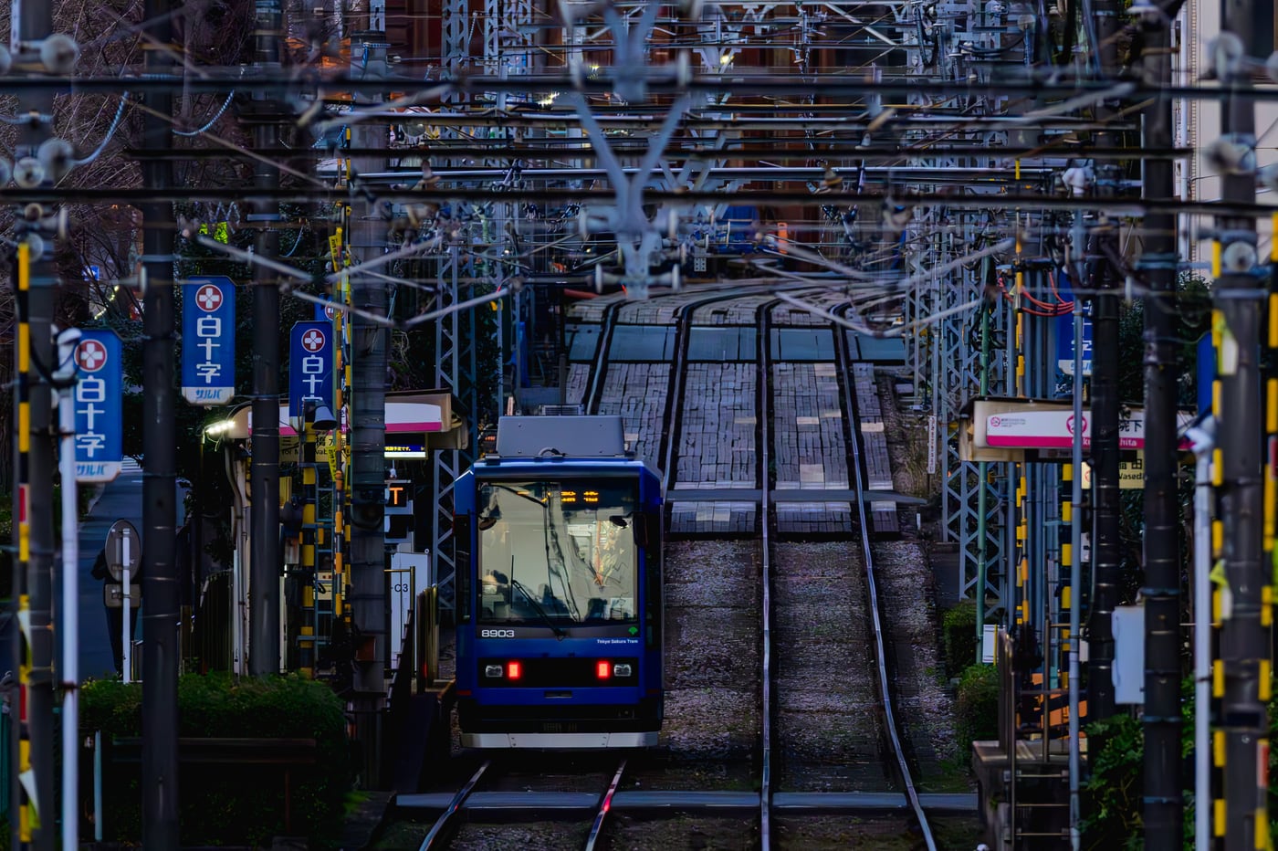 A blue tram running beneath overhead wires on tracks leading toward the slope