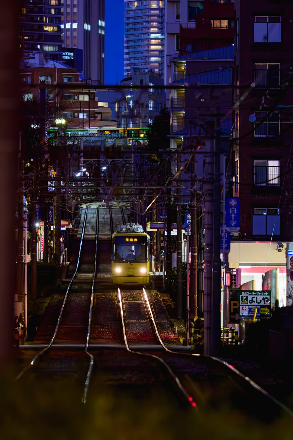 A distant tram approaching along the slope beneath a deep blue evening sky and high-rise buildings